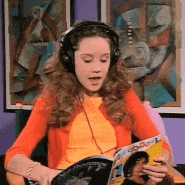 a young woman wearing headphones is reading a magazine .