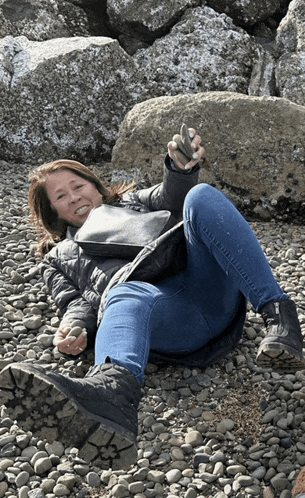 a woman is laying on a rocky beach holding a rock in her hand
