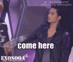 a man in a black jacket says come here in front of a purple wall