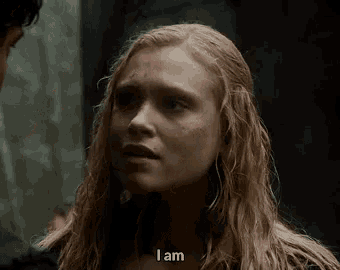 a woman with long blonde hair is talking to a man in a dark room and says `` i am '' .