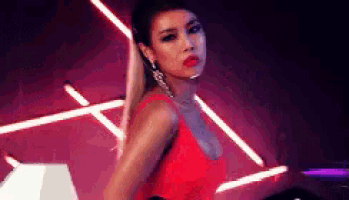 a woman in a red dress is standing in a dark room with neon lights .