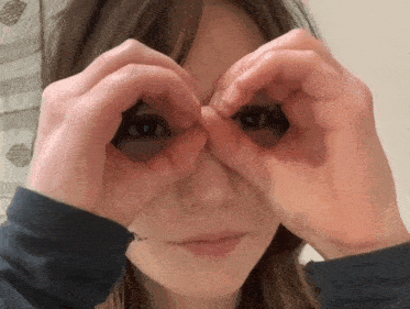 a woman making a heart shape with her hands over her eyes