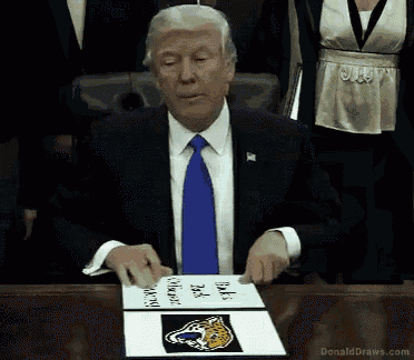 donald trump is sitting at a table with a sign on it that says back to the wildcats