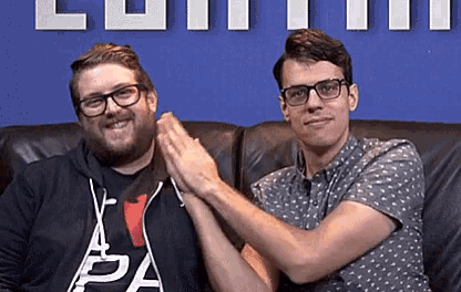 two men are sitting next to each other on a couch and giving each other a high five .