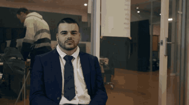 a man in a suit and tie is sitting in front of a glass door with a list of numbers on it