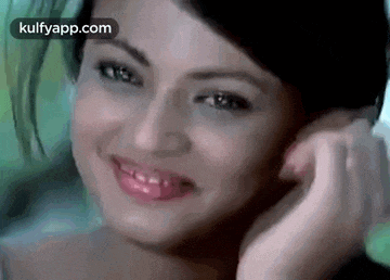 a close up of a woman 's face with her hand on her ear and smiling .