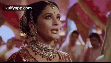 a woman in a wedding dress and jewelry is standing in front of a crowd of people .