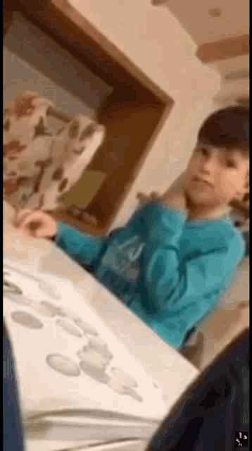 a young boy in a blue shirt is sitting at a table