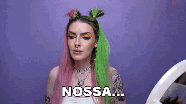 a woman with pink and green hair is looking at herself in a mirror and saying nossa .