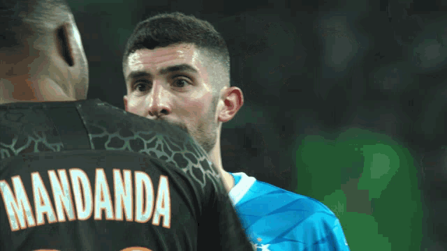 a man in a mandanda jersey talks to another man in a blue jersey