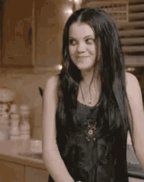 a young woman with long black hair is standing in a kitchen .