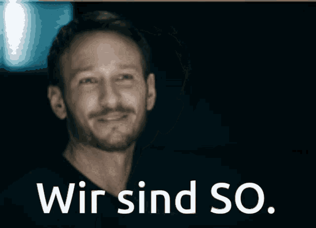 a man with a beard is giving a thumbs up with the words wir sind so behind him