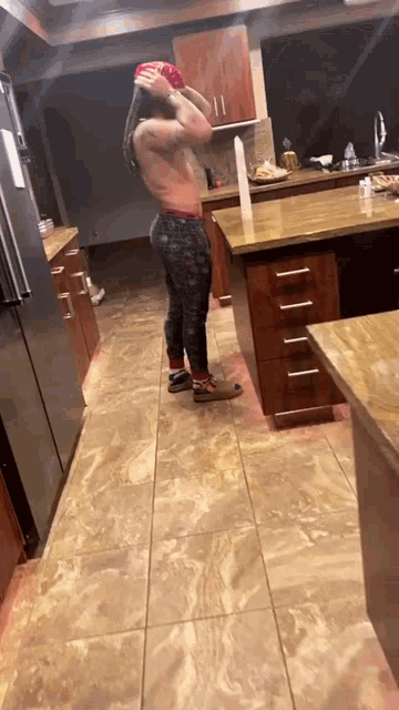 a man without a shirt is standing in a kitchen holding a red ball .