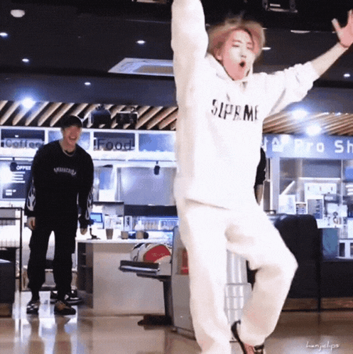 a man in a supreme hoodie is dancing in a bowling alley while another man watches .