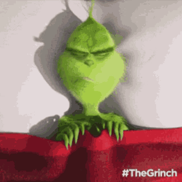 the grinch from the movie the grinch is laying under a red blanket with his eyes closed .