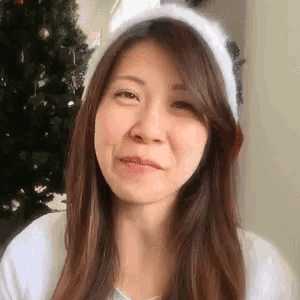 a woman wearing a white hat and a white shirt is making a funny face in front of a christmas tree .
