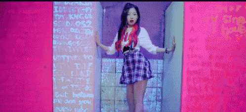 a girl with red hair and a plaid skirt is standing in front of a wall with graffiti on it .