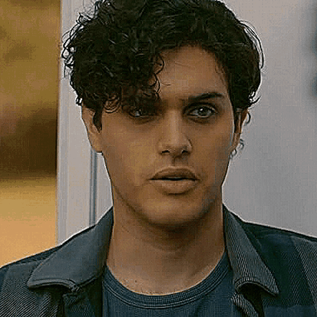 a close up of a man with curly hair wearing a blue shirt and jacket .