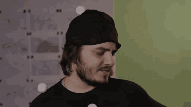 a man with a beard wearing a black hat and a black shirt is holding a ball .