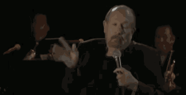 a man singing into a microphone in a dark room with a band behind him