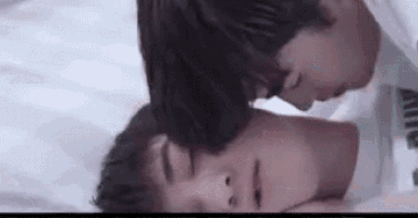 a couple of men are laying on a bed and kissing each other .
