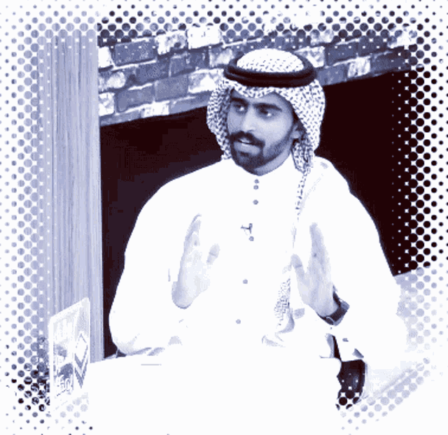 a man with a beard wearing a white shirt and a head scarf is sitting at a table