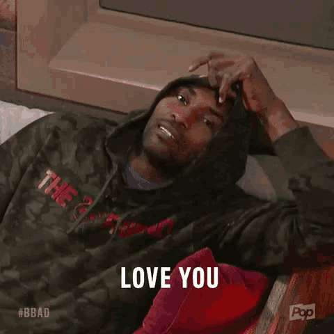 a man in a hoodie is laying on a bed with his hand on his head and says `` love you '' .
