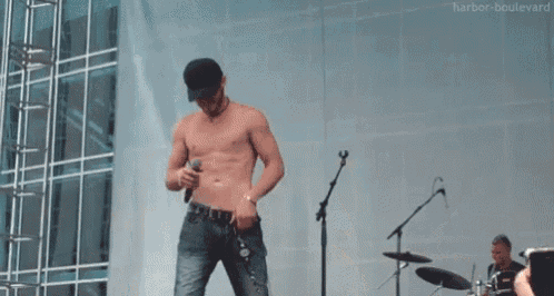 a shirtless man is standing on a stage holding a microphone while a crowd watches .