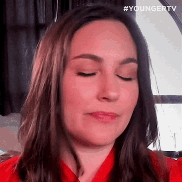 a close up of a woman 's face with her eyes closed and a red shirt on .