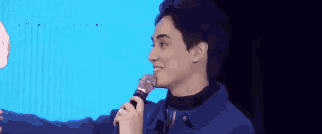 a man in a blue jacket is holding a microphone in his mouth and smiling .