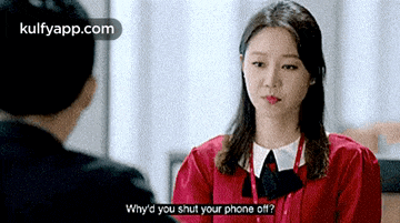 a woman in a red shirt is talking to a man in a suit and asking him to shut his phone off .