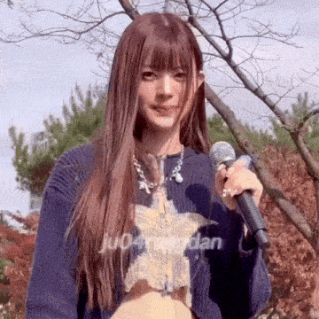 a woman in a blue sweater is holding a microphone in front of trees .