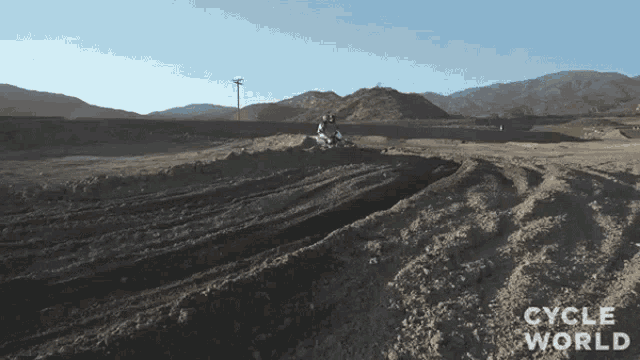a person riding a dirt bike on a dirt road with the words cycle world on the bottom right
