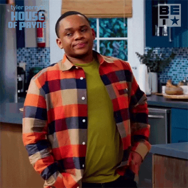 a man wearing a plaid shirt and a green shirt is standing in a kitchen .