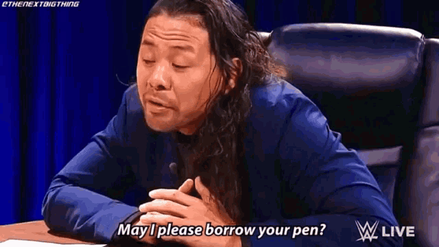 a man in a blue suit is sitting at a table and saying `` may i please borrow your pen? ''