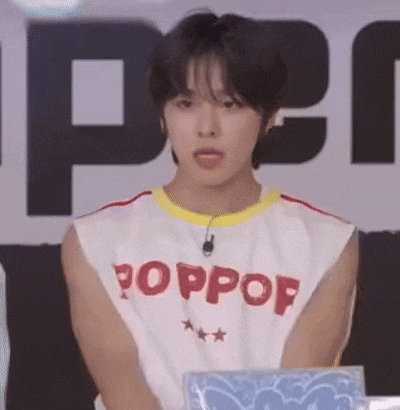 a young man wearing a white tank top with the word poppop on it is sitting in front of a microphone .