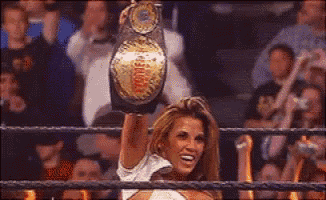 a woman in a wrestling ring holds up a world heavyweight championship