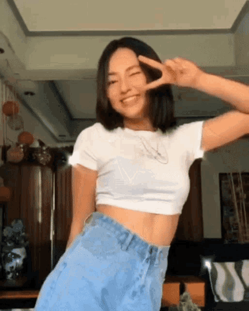 a woman in a white crop top and blue shorts is giving a peace sign .