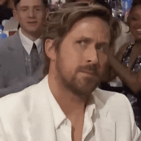 a man with a beard is sitting in a crowd of people making a funny face .