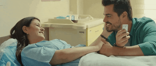 a man is holding the hand of a pregnant woman who is laying in a hospital bed