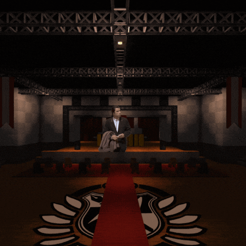 a man in a suit is sitting on a stage with a red carpet and a logo on the floor
