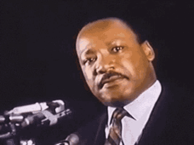 martin luther king jr. is standing in front of a microphone .