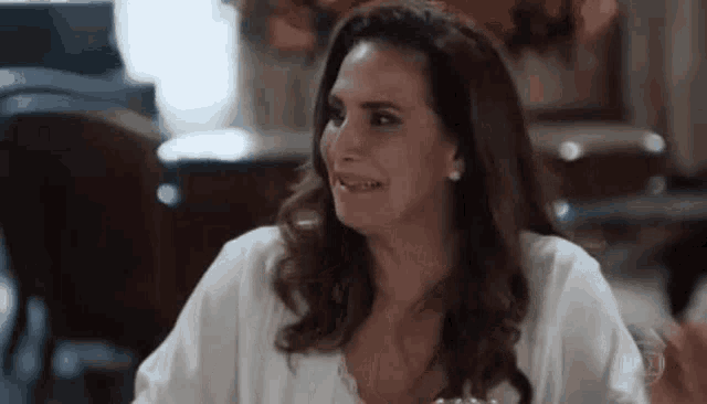 a woman is sitting at a table in a restaurant with a glass of wine and making a funny face .
