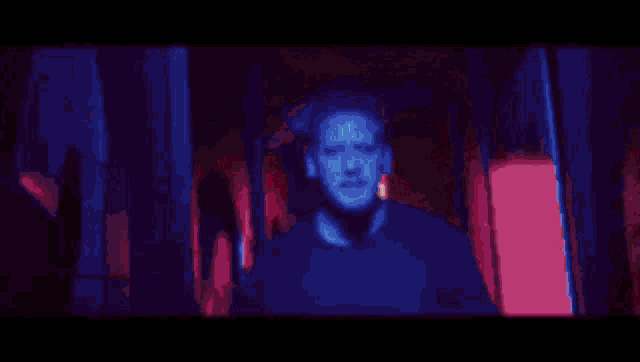 a man in a red and white jacket is standing in a dark room with red lights behind him .