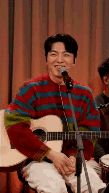 a man in a colorful sweater is playing a guitar and singing into a microphone