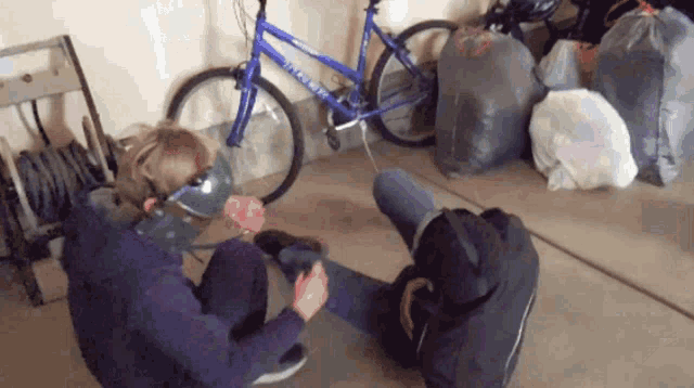 a person wearing a mask is sitting on the floor in front of a blue bike