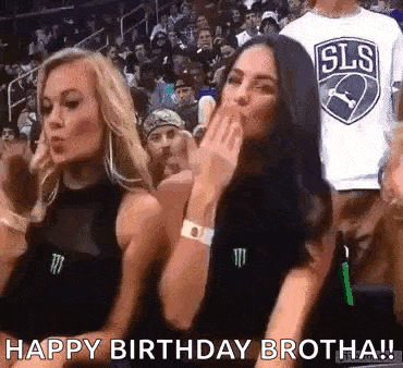 two women are blowing a kiss at a basketball game while a man in a sls shirt looks on .
