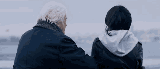 a man and a woman are sitting on a bench looking out over the water