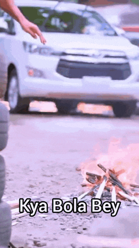 a white car is driving past a fire with the words kya bola bey written on the ground