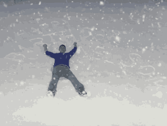 a man in a blue sweater is laying in the snow with his arms in the air
